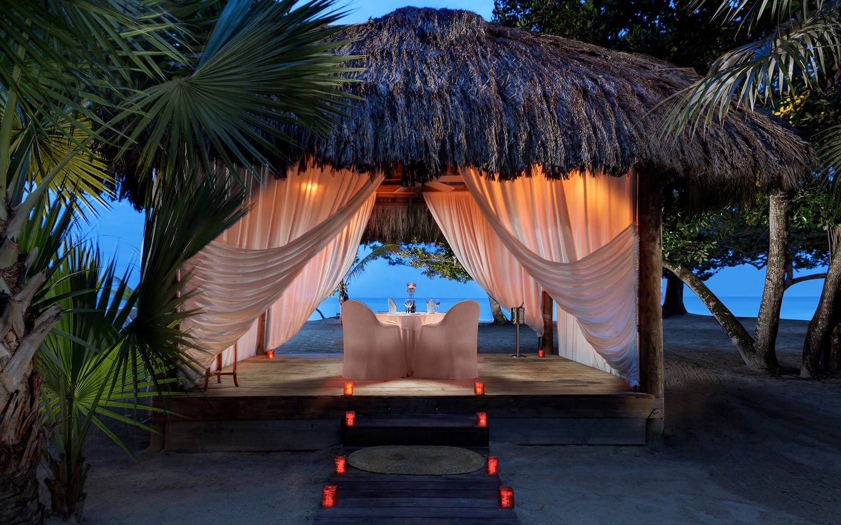 private dining table under a tiki hut on the beach at night
