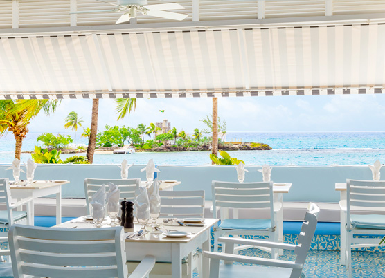 striped awning covering a casual patio dining area overlooking the ocean