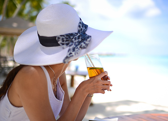 woman sipping tea wearing a white wide brim hat on the beach
