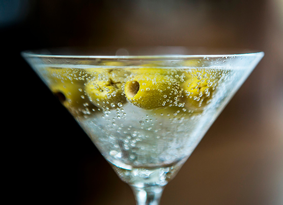 close up of a martini filled with green olives